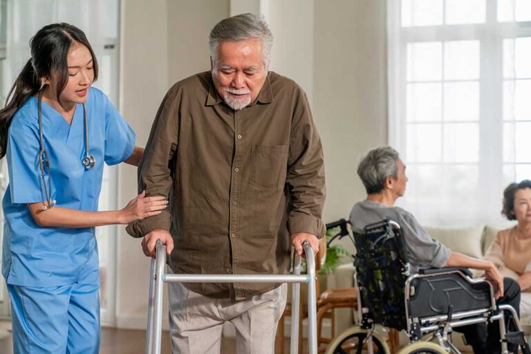 Older adults share a meal and conversation around a table in a bright assisted living dining room.