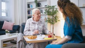 Older adult choosing clothing beside a caregiver in a bright assisted living room.